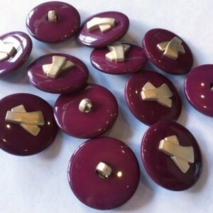 May include: Twelve burgundy buttons with gold accents. The buttons have a flat, round shape and a shiny finish.
