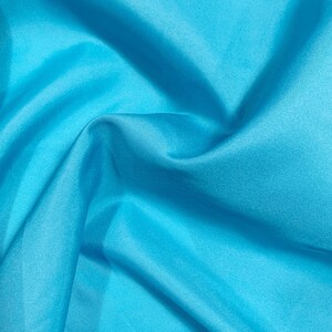 May include: A close-up of a smooth, light blue fabric with soft folds and wrinkles.