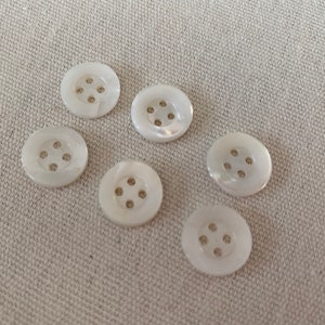 May include: Six white round buttons with four holes each. The buttons are made of a pearly material.
