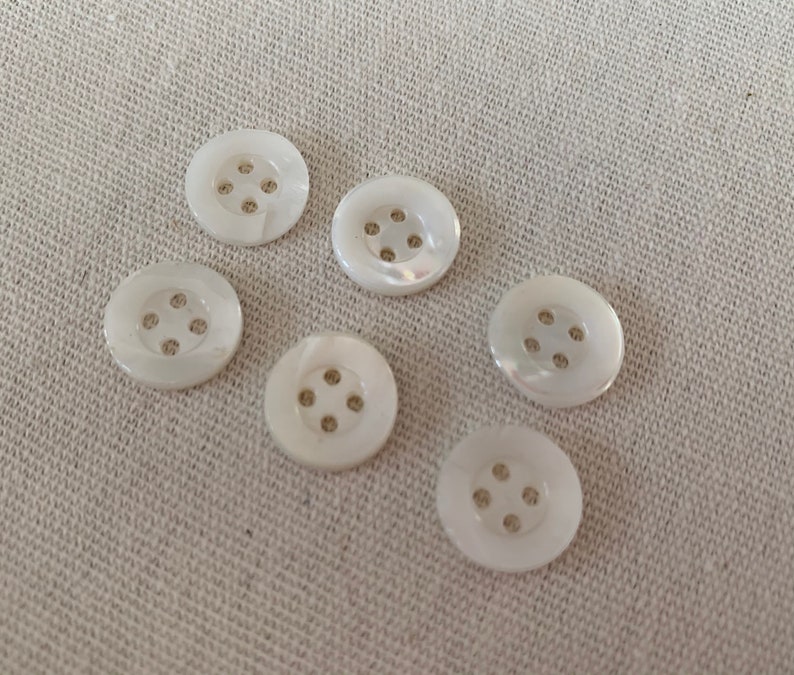 May include: Six white round buttons with four holes each. The buttons are made of a pearly material.
