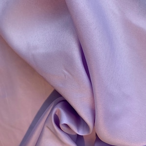 May include: A close-up of a soft, smooth, lavender fabric with a subtle sheen. The fabric is draped and folded, creating a luxurious and elegant look.