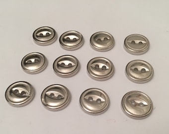 May include: Twelve silver-toned buttons with two holes each. The buttons are round and have a slightly raised edge.
