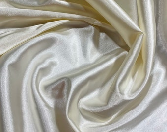 Könnte beinhalten: Nahaufnahme eines glatten, elfenbeinfarbenen Satin-Stoffes mit weichen, fließenden Falten.
