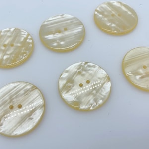 以下が含まれることがあります： 真珠のような光沢のある白とクリーム色の丸いボタンが6つ。ボタンには穴が2つ開いています。