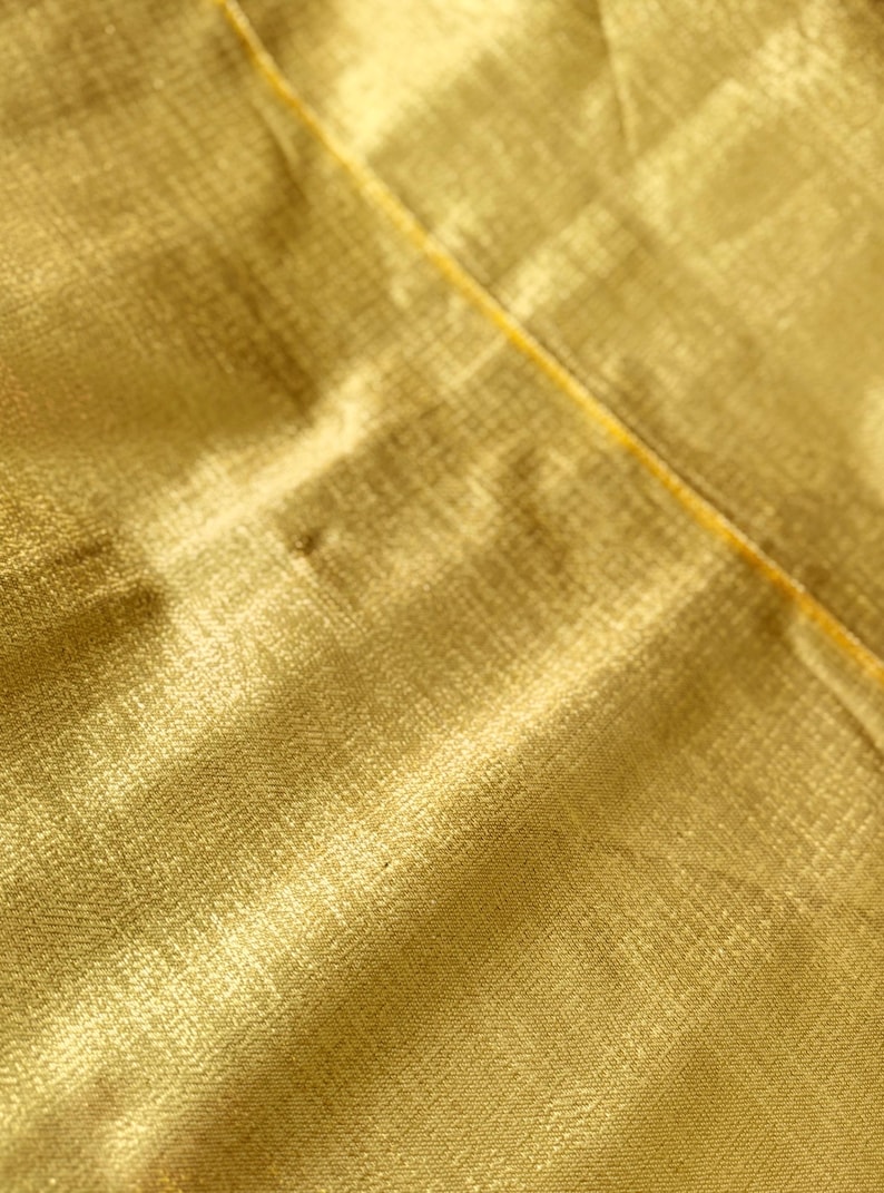 Puede incluir: Primer plano de una tela amarillo dorado con un patr&oacute;n sutil y texturizado. Una fina costura amarilla atraviesa la imagen en diagonal. La tela tiene un ligero brillo, lo que sugiere un material lujoso.