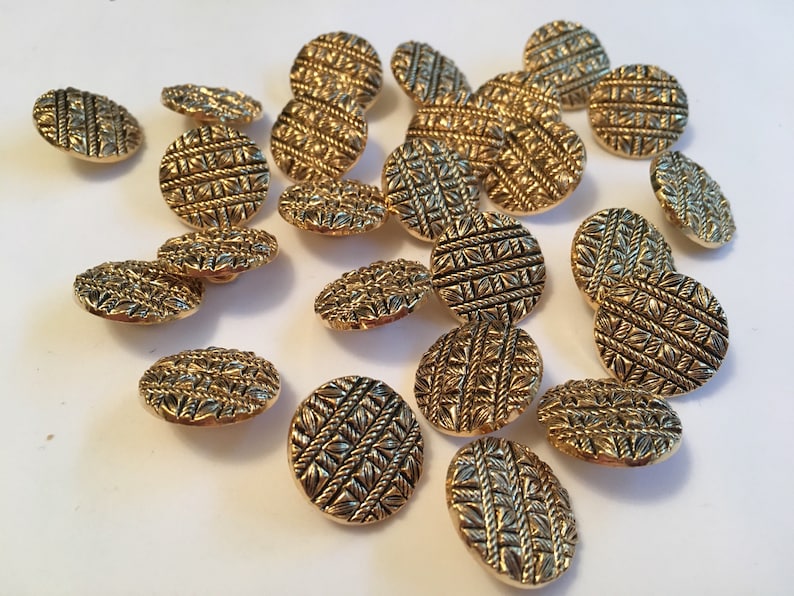 May include: A collection of 18 gold-tone buttons with a woven design. The buttons are round and have a raised, textured surface.