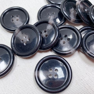 May include: A collection of black and white buttons with a glossy finish. The buttons have four holes and a raised rim.
