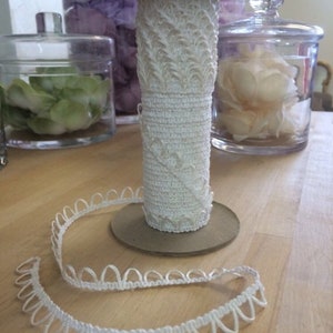 May include: White crocheted trim with a scalloped edge. The trim is wound around a cardboard spool.