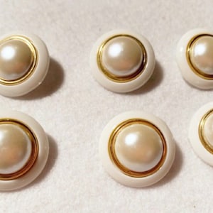 May include: Six white pearl buttons with a gold trim. The buttons are round and have a raised pearl center.