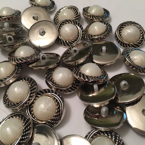 May include: A pile of silver and white pearl buttons with a rope-like design around the edge.