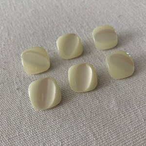 May include: Six off-white, square-shaped buttons with a pearlescent finish.