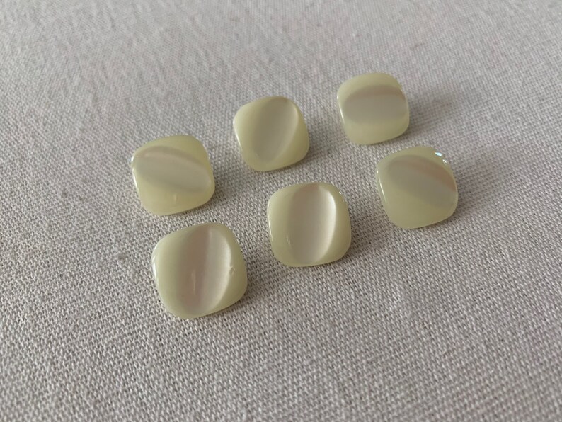 May include: Six off-white, square-shaped buttons with a pearlescent finish.