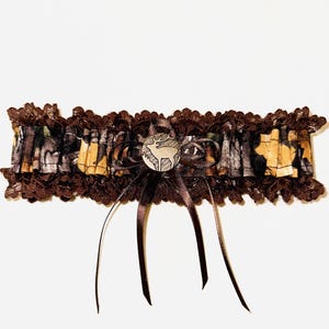 May include: A brown lace garter with a camouflage pattern and a silver-tone deer emblem. The garter features a dark brown satin bow and is designed with a woodland theme.