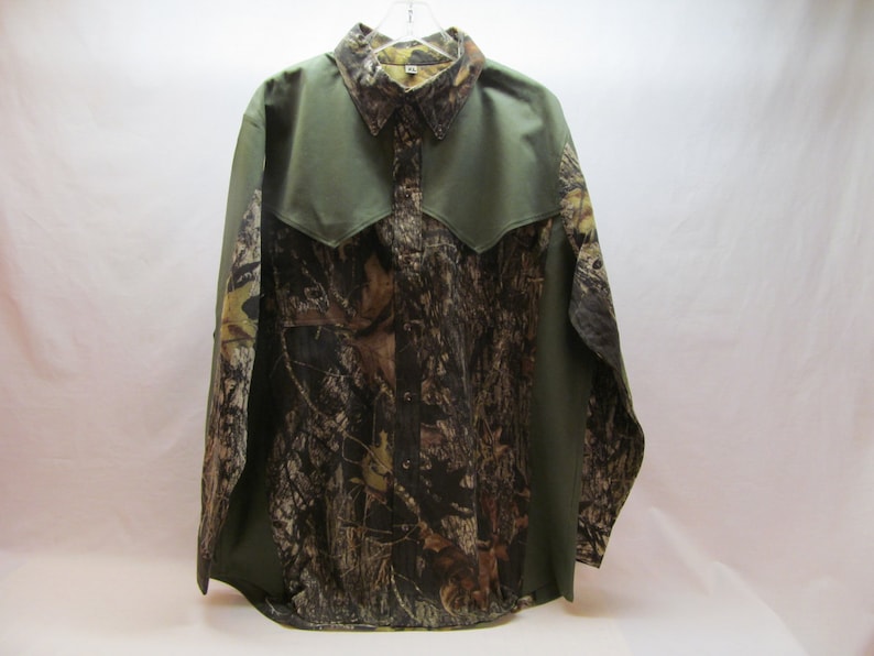 Puede incluir: Una camisa de manga larga con botones de color verde y camuflaje con un yugo y un cuello puntiagudo.