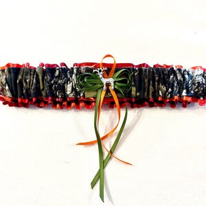 May include: A red, orange, and green garter with a camouflage pattern and a silver deer charm.