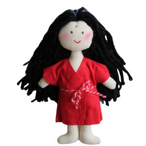 May include: A handmade doll with long black yarn hair, wearing a red kimono with a white and red sash. The doll has a white face with pink cheeks and a simple smile.