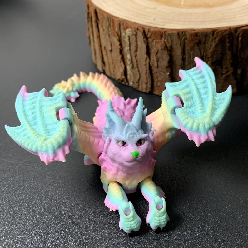 May include: A colorful, 3D-printed dragon figurine in pastel shades of pink, blue, yellow, and green. The dragon has large, wing-like appendages and a long, segmented tail. The dragon's head features horns and green eyes.