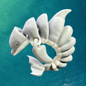 Könnte beinhalten: Graue, 3D-gedruckte, bewegliche Delfinskulptur. Das Design zeigt einen segmentierten Körper, eine gebogene Schwanzflosse und eine spitze Rückenflosse. Die Skulptur ist vor einem türkisfarbenen Hintergrund platziert.