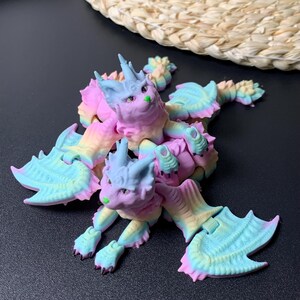May include: A colorful, fantasy creature figurine with a cat-like face and bat-like wings. The figurine is a mix of pastel colors, including pink, blue, yellow, and green. The creature has a whimsical design, with pointed ears and a spiky crown.