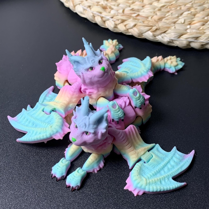 May include: A colorful, fantasy creature figurine with a cat-like face and bat-like wings. The figurine is a mix of pastel colors, including pink, blue, yellow, and green. The creature has a whimsical design, with pointed ears and a spiky crown.