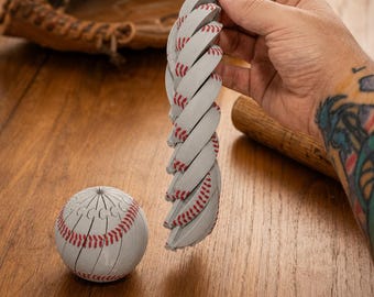 Könnte beinhalten: Ein weißer Baseball mit roten Nähten, der ein einzigartiges segmentiertes Design aufweist, das es ermöglicht, ihn in eine lange, flexible, spiralförmige Kette aus verbundenen Teilen zu ziehen, neben einem vollständigen, kugelförmigen Baseballmodell.