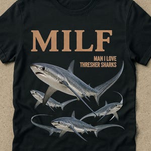 May include: Black t-shirt with the word "MILF" in brown capital letters above a graphic of several thresher sharks. The text "MAN I LOVE THRESHER SHARKS" is below the word "MILF". The word "black" is in the bottom right corner.