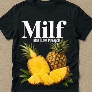 Puede incluir: Camiseta negra con la palabra "Milf" en letras blancas grandes sobre la frase "Man I Love Pineapple". La camiseta presenta un gráfico de una piña entera, una mitad de piña y rodajas de piña.