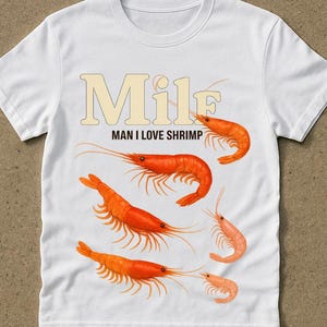 May include: White t-shirt with the text "MILF MAN I LOVE SHRIMP" in beige letters. The shirt features illustrations of orange shrimp. The word "white" is printed in the bottom right corner.