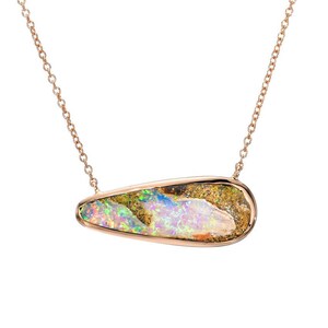 May include: A delicate gold chain necklace with a teardrop-shaped opal pendant. The opal has a rainbow of colors, including green, blue, and purple. A small diamond accents the chain.