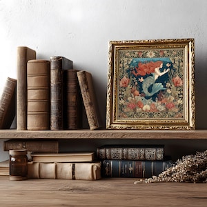 K&ouml;nnte beinhalten: Ein gerahmter Wandteppich mit einer Meerjungfrau-Illustration. Das Kunstwerk zeigt eine Meerjungfrau mit roten Haaren und blauem Schwanz, umgeben von Korallen und Fischen. Der Rahmen ist goldfarben, und der Wandteppich wird auf einem Holzregal mit antiken B&uuml;chern ausgestellt.