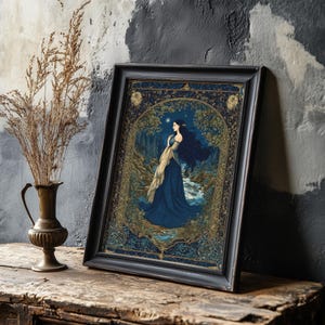 May include: A framed art print depicting a woman in a blue gown by a river in a forest. The artwork uses a dark blue and gold palette, set in a black frame. A vase with dried plants is positioned to the left of the framed print.
