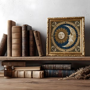 May include: A square framed artwork featuring a central circular illustration of a sun and moon with human faces, surrounded by a blue and gold celestial pattern. The frame is ornate, metallic gold, and rectangular with intricate embossed detailing.