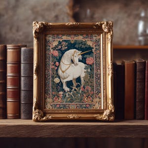 May include: A framed tapestry featuring a white unicorn with a golden horn and collar, set against a backdrop of flowers and foliage. The ornate gold frame sits on a wooden shelf with antique books.
