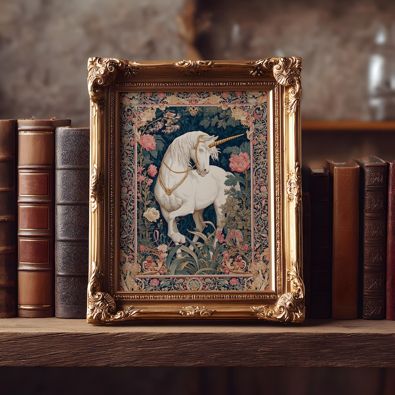 May include: A framed tapestry featuring a white unicorn with a golden horn and collar, set against a backdrop of flowers and foliage. The ornate gold frame sits on a wooden shelf with antique books.
