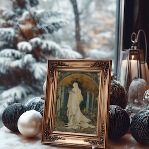 Op de afbeelding: Een ingelijst kunstwerk met een gouden, sierlijke lijst toont een vrouw in een witte jurk in een bosrijke omgeving. Het kunstwerk staat op een houten oppervlak met decoratieve zwarte en witte ornamenten, met een besneeuwde sc&egrave;ne zichtbaar door een raam.