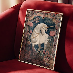 May include: A framed print featuring a white unicorn with a golden horn and bridle, set against a backdrop of floral and foliage patterns. The artwork is in a gold frame and rests on a red velvet surface.