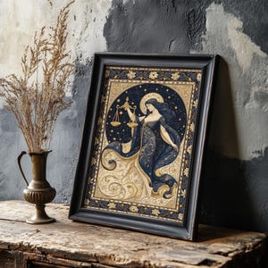 May include: Framed art print featuring a celestial illustration of the Libra zodiac sign. The artwork depicts a woman holding scales, set against a starry night sky and ornate gold and blue details. The frame is black.