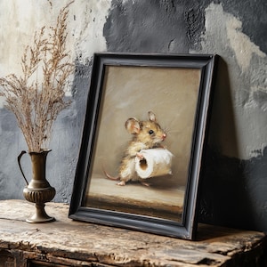 May include: A framed oil painting depicting a small brown mouse standing on a wooden surface while holding a roll of white toilet paper. The artwork is enclosed in a simple black frame, showcasing a neutral beige background and detailed brushwork.