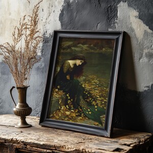 May include: A framed print of a Pre-Raphaelite painting. The artwork depicts a woman in a dark green dress with gold accents, seated near a body of water. The frame is black, and the overall aesthetic is vintage.