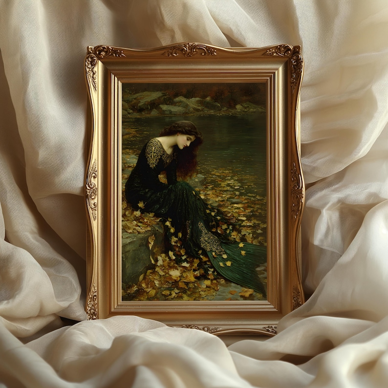 May include: A framed print of a woman in a dark green dress sitting by a body of water. The gold frame surrounds the artwork, which features a woman with long, dark hair and a flowing gown. The scene is set in a natural environment with autumn leaves.