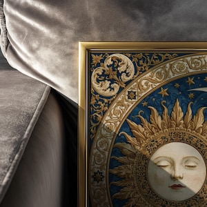 May include: A framed wall art print featuring a central sun face with closed eyes, surrounded by intricate gold and blue decorative scrollwork, star motifs, and a crescent moon, all encased in a thin, metallic gold-colored rectangular frame.