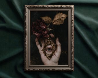 May include: A framed wall art print featuring a hand holding a small, ornate gold oval frame containing a realistic human eye. Above the hand, a dark, withered red rose with brown leaves is visible against a dark, moody background.