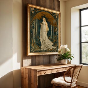 Op de afbeelding: Een ingelijste kunstdruk met een vrouw in een vloeiende witte jurk, tegen een bosachtergrond met gouden en blauwgroene accenten. Het kunstwerk bevindt zich in een gouden, sierlijke lijst, gemonteerd op een houten muur boven een houten bureau.