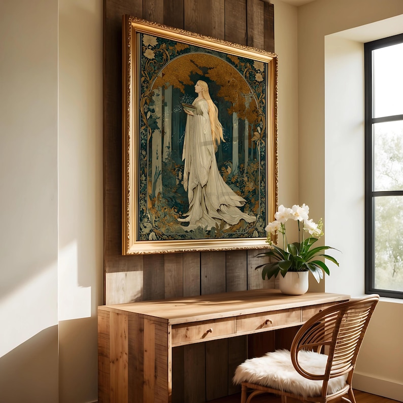 Op de afbeelding: Een ingelijste kunstdruk met een vrouw in een vloeiende witte jurk, tegen een bosachtergrond met gouden en blauwgroene accenten. Het kunstwerk bevindt zich in een gouden, sierlijke lijst, gemonteerd op een houten muur boven een houten bureau.