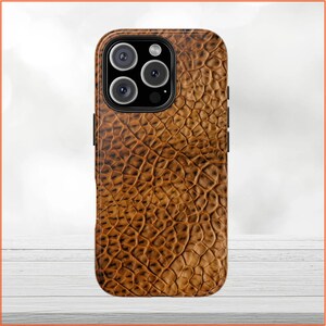 Può includere: Una custodia per telefono in pelle marrone con un motivo a pelle di coccodrilo. La custodia ha un ritaglio per la fotocamera nero con tre obiettivi.