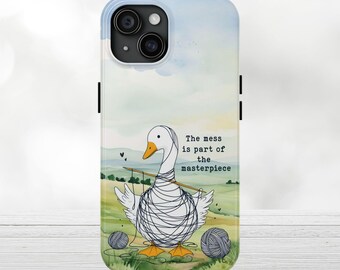 May include: A phone case featuring a whimsical illustration of a white goose tangled in yarn, with the text "The mess is part of the masterpiece." The background depicts a green field and blue sky.