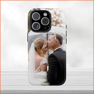 May include: A white and black phone case with a photo of a couple kissing under an umbrella. The couple is dressed in formal attire, and the woman is wearing a white wedding dress.