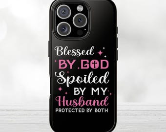 Op de afbeelding: Zwarte telefoonhoes met de tekst "Blessed by God, Spoiled by my Husband, Protected by Both" in wit en roze. Het ontwerp bevat een kruissymbool. De hoes heeft een glanzende afwerking.