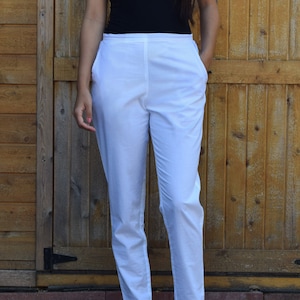 May include: White cotton pants with a straight leg fit. The pants have a simple design and are a versatile piece of clothing.