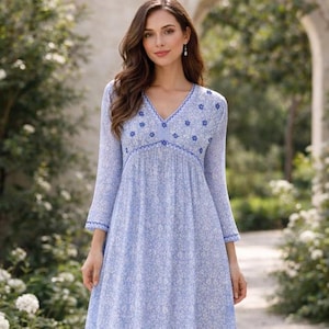 May include: A light blue floral print dress with long sleeves and a V-neckline. The dress features delicate blue floral embroidery around the neckline and sleeves. The dress is made of a soft, flowing fabric.